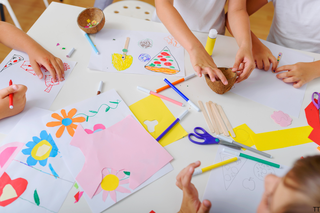 children's hands at table making flowers with coloured paper